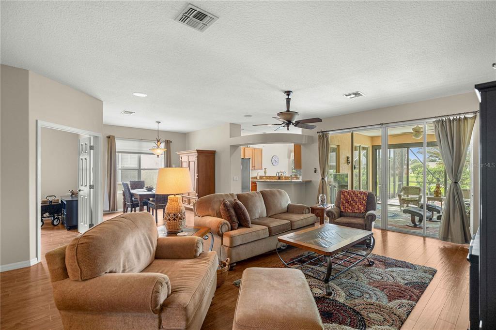 A living room with wood-look flooring, a ceiling fan, and sliding glass doors to a patio — 15862 SW 13TH CIRCLE, OCALA, FL