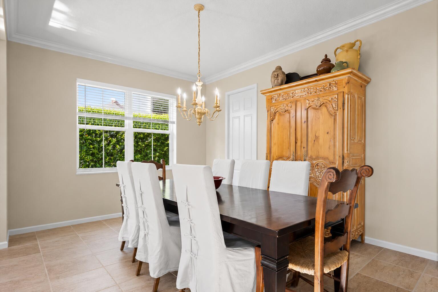 A dining room features a dark wood table, white slipcovered chairs, and a large armoire — 464 Oriole Lane, Jupiter FL 33458, JUPITER, FL