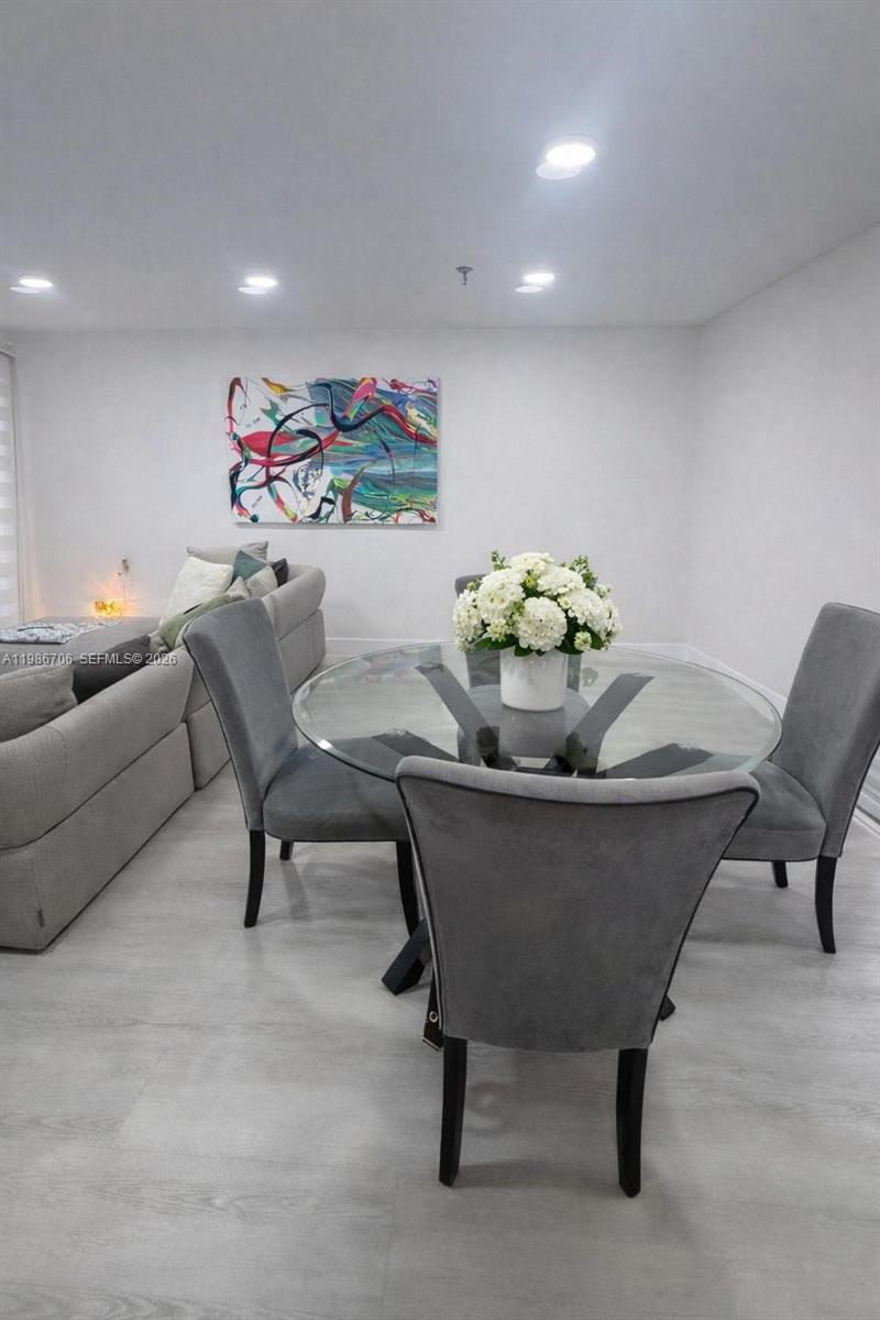A dining area with a glass-topped table and gray chairs sits beside a living room — 671 NE 195th St, Miami FL 33179, MIAMI, FL