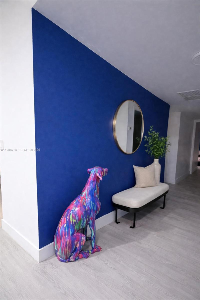 A vibrant blue accent wall features a colorful dog sculpture, a bench, and a mirror — 671 NE 195th St, Miami FL 33179, MIAMI, FL