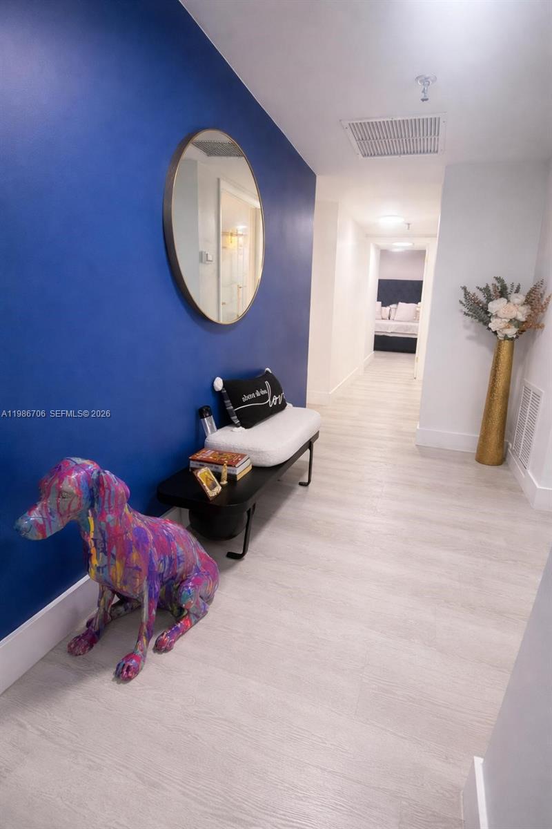 A hallway features a blue accent wall, a bench, a mirror, and a colorful sculpture — 671 NE 195th St, Miami FL 33179, MIAMI, FL
