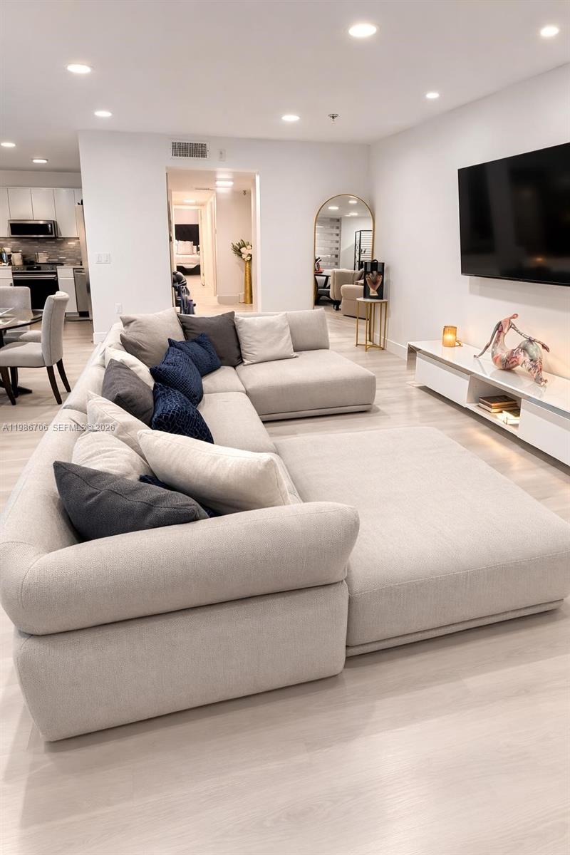 A modern living room features a large beige sectional sofa facing a wall-mounted television — 671 NE 195th St, Miami FL 33179, MIAMI, FL