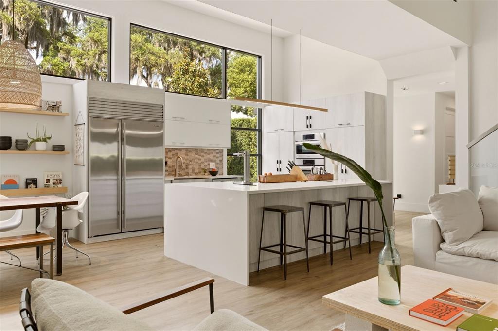 A modern kitchen features white cabinetry, a large island with bar seating, and stainless appliances — 446 MELROSE AVENUE, WINTER PARK, FL