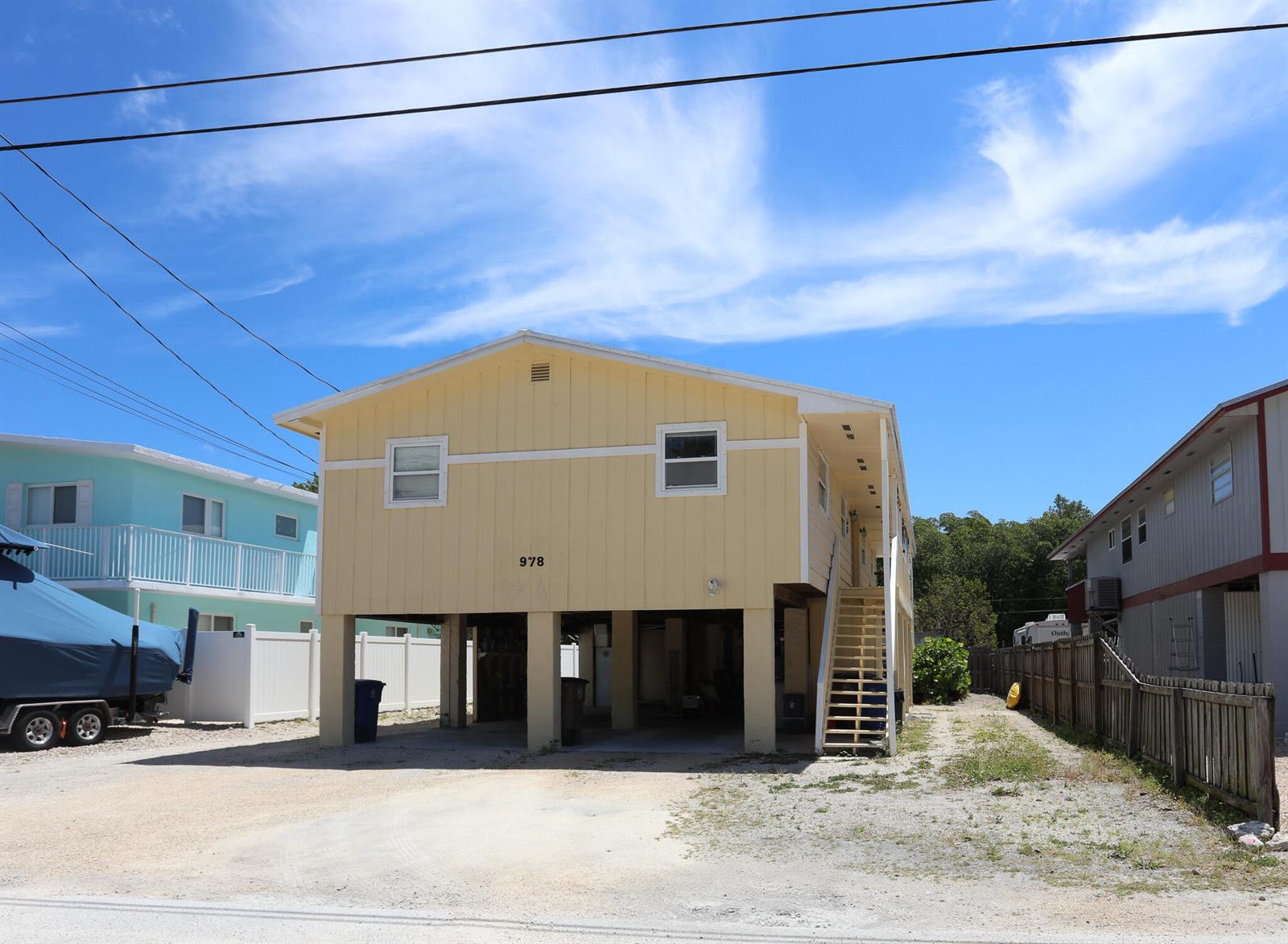 A yellow elevated house with a staircase stands between two other homes under a sky — 978 Gibraltar Road, Key Largo FL 33037, KEY LARGO, FL