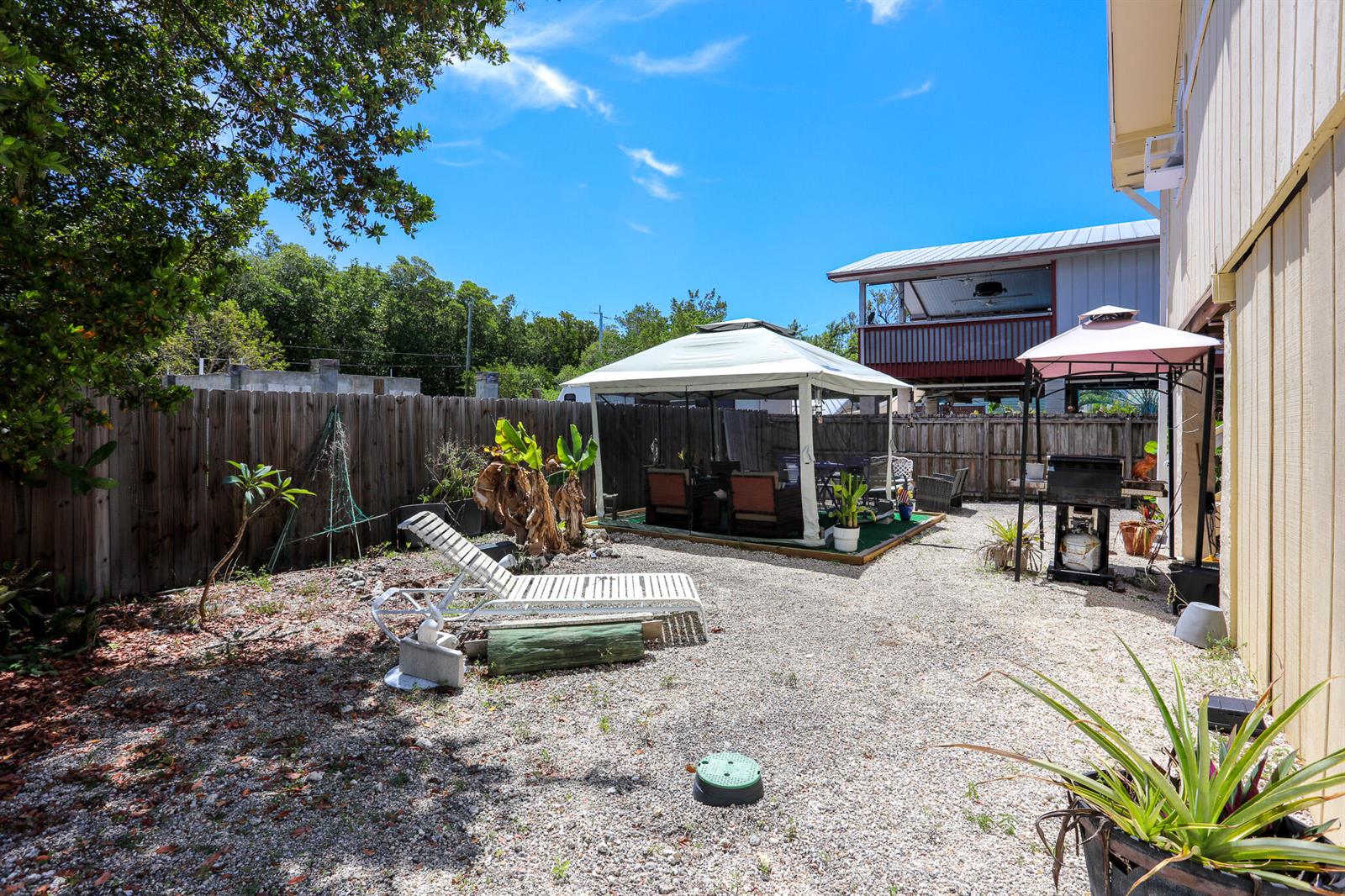 A gravel backyard features a gazebo, a lounge chair, and a grill under a canopy — 978 Gibraltar Road, Key Largo FL 33037, KEY LARGO, FL