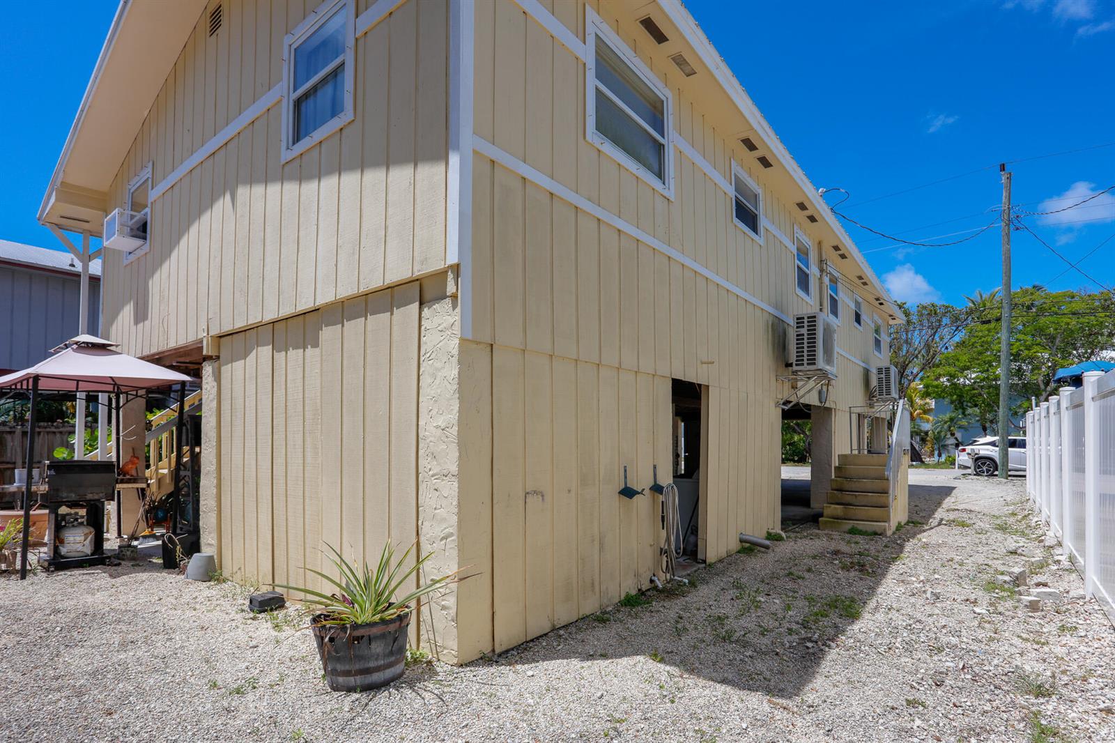 The exterior of a yellow, elevated house features vertical siding, a gravel yard, and stairs — 978 Gibraltar Road, Key Largo FL 33037, KEY LARGO, FL
