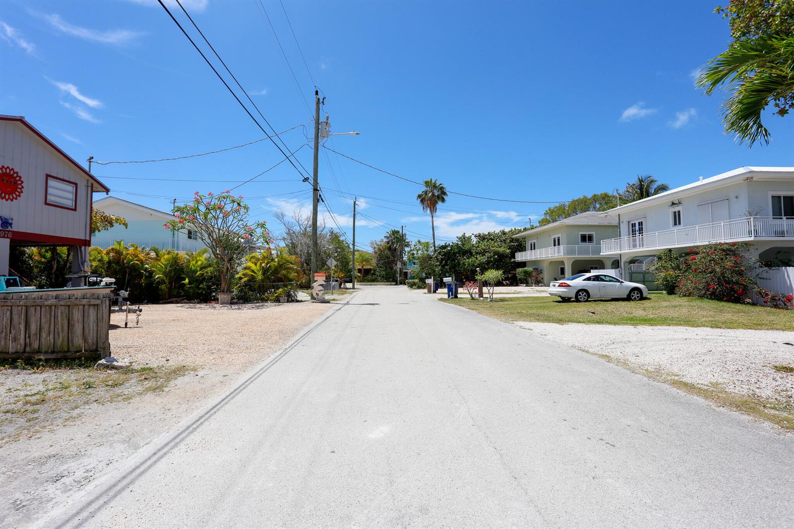 A paved street runs between residential houses with palm trees and a white car parked — 978 Gibraltar Road, Key Largo FL 33037, KEY LARGO, FL