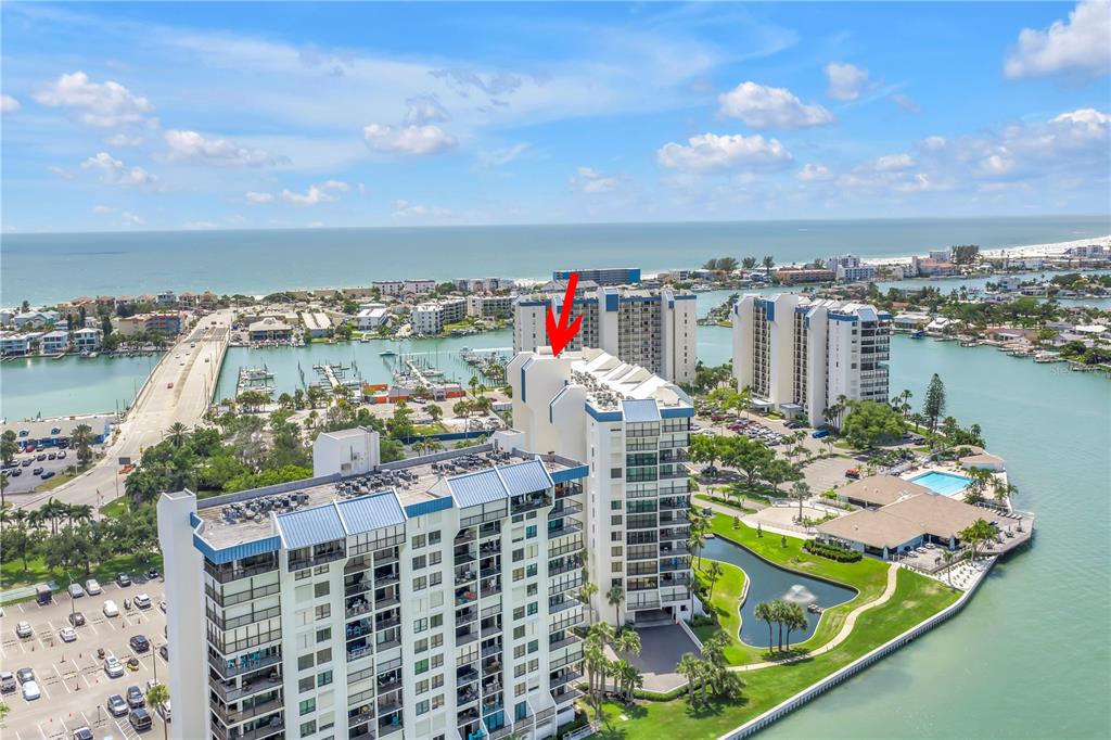 An aerial view shows a multi-story waterfront condominium complex with a red arrow pointing to the roof — 9425 BLIND PASS ROAD UNIT 207, ST PETE BEACH, FL