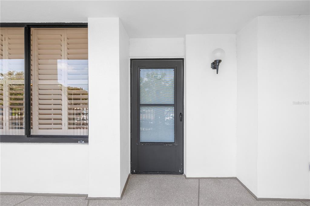 A white exterior wall features a dark-framed glass door labeled 207 and a window — 9425 BLIND PASS ROAD UNIT 207, ST PETE BEACH, FL