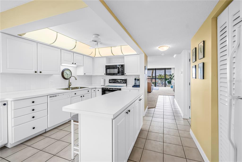 A white kitchen with an island, tile floors, and a view into the living area — 9425 BLIND PASS ROAD UNIT 207, ST PETE BEACH, FL
