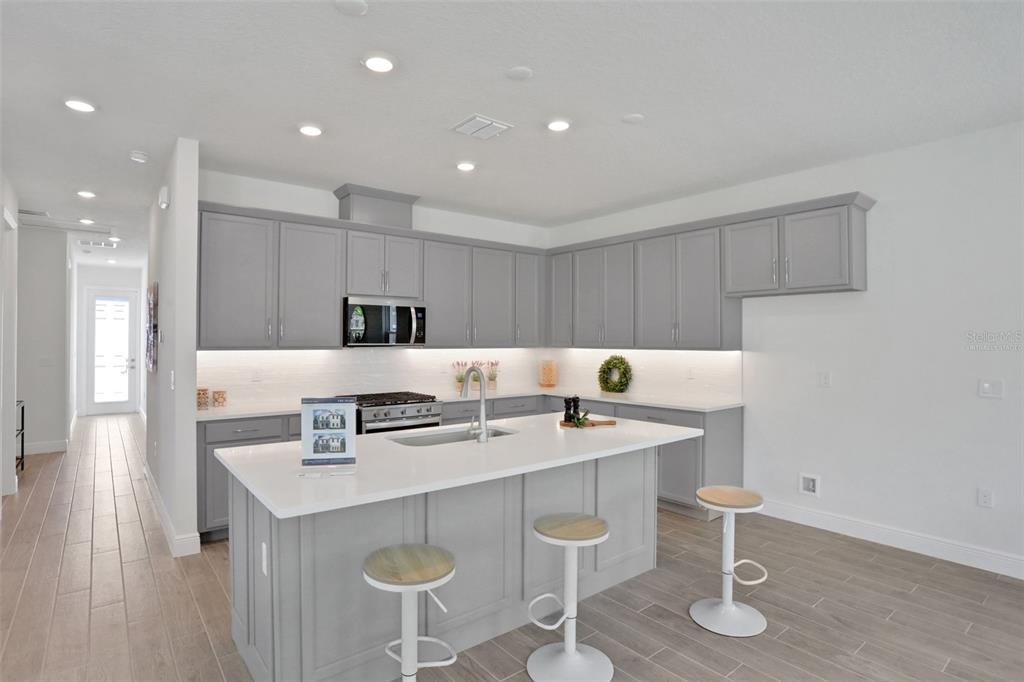 A modern kitchen features gray cabinets, a white quartz island, and light wood-look tile flooring — 9135 WALCOTT LANE, LAKEWOOD RANCH, FL