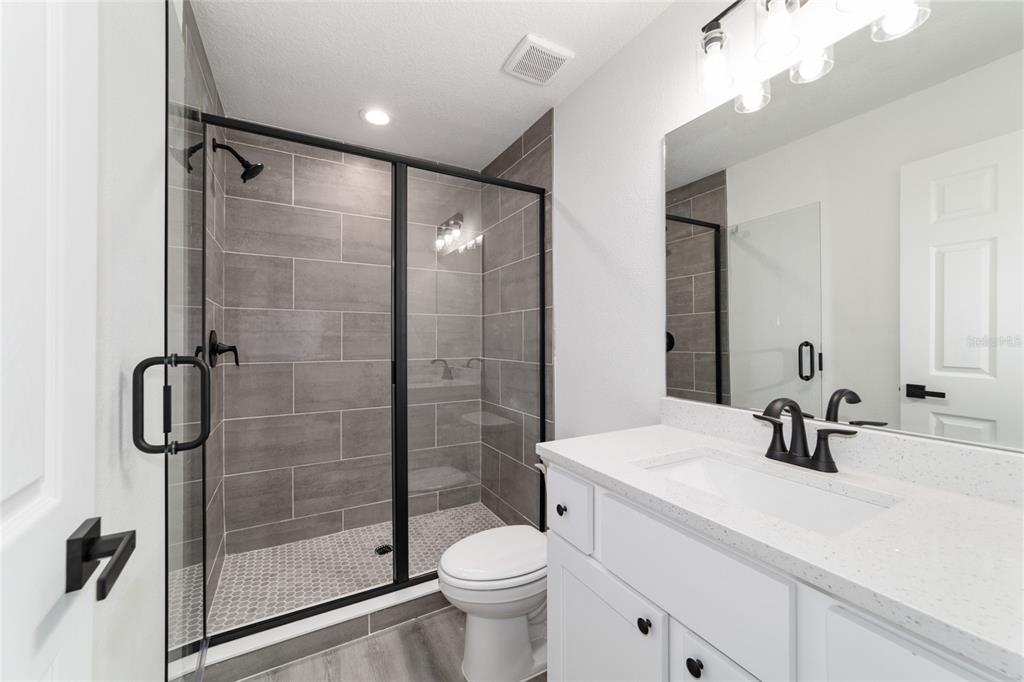 A modern bathroom features a glass-enclosed shower with gray tile, a white vanity, and toilet — 22632 SW NAUTILUS BOULEVARD, DUNNELLON, FL