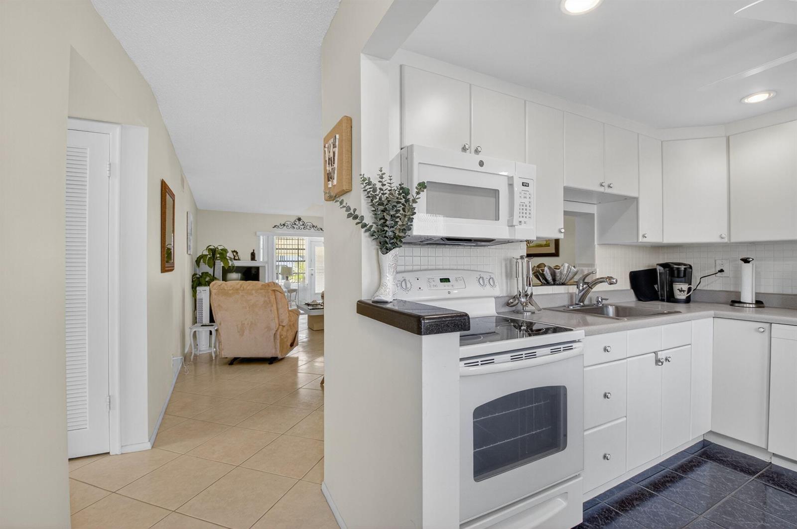 A white kitchen with a stove and microwave opens into a living room with tile floors — 2152 NE 1st Way # 101, Boynton Beach FL 33435, BOYNTON BEACH, FL