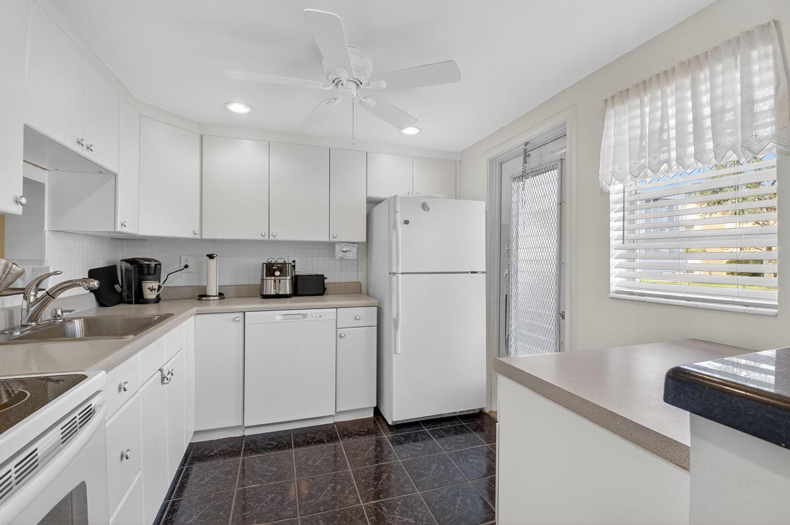 A kitchen with white cabinets, dark tiled floors, a white refrigerator, and a window — 2152 NE 1st Way # 101, Boynton Beach FL 33435, BOYNTON BEACH, FL