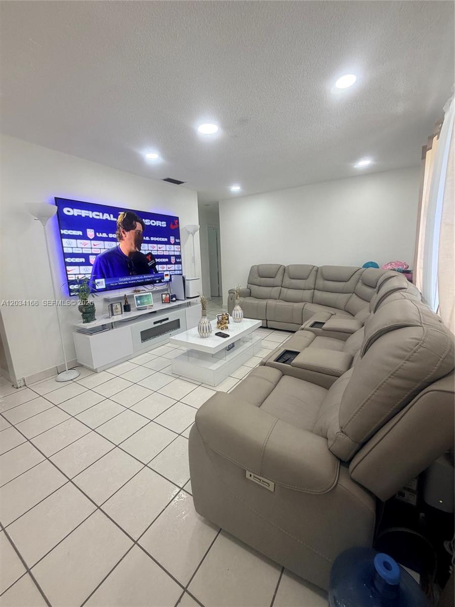 A living room features a large sectional sofa, a white media console, and a wall-mounted television — 3821 SW 89th Ct, Miami FL 33165, MIAMI, FL