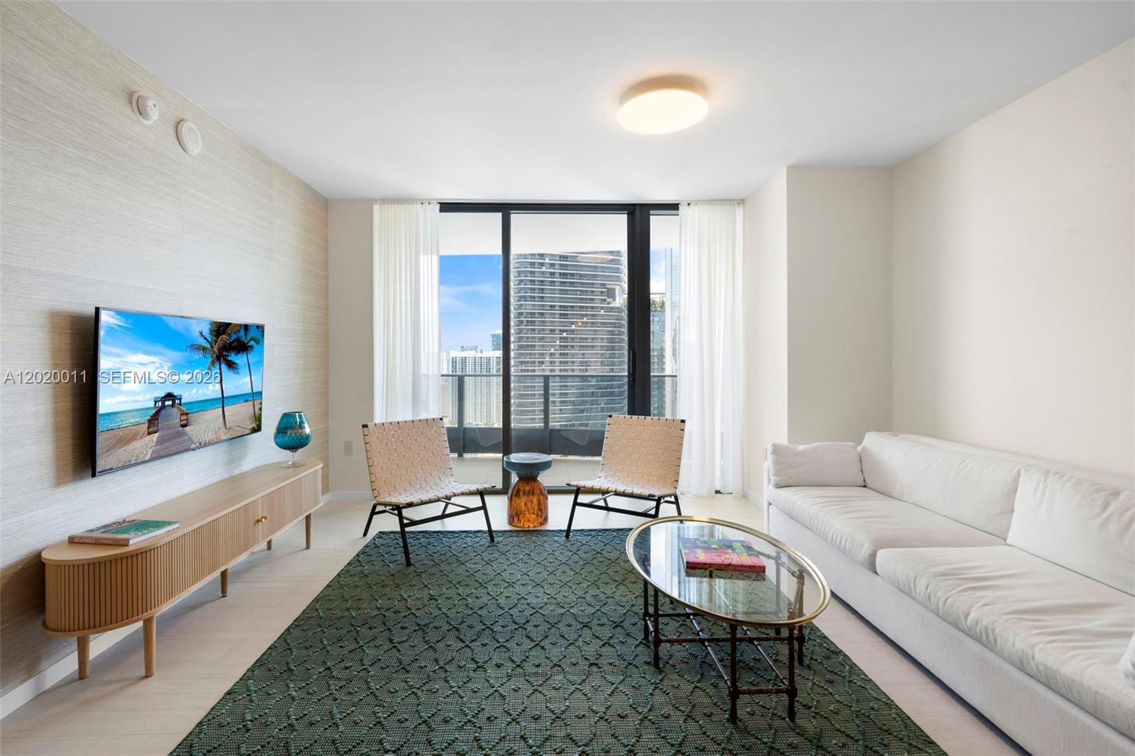 A modern living room features a white sofa, two woven chairs, and a glass coffee table — 1000 Brickell Plz # 4014, Miami FL 33131, MIAMI, FL