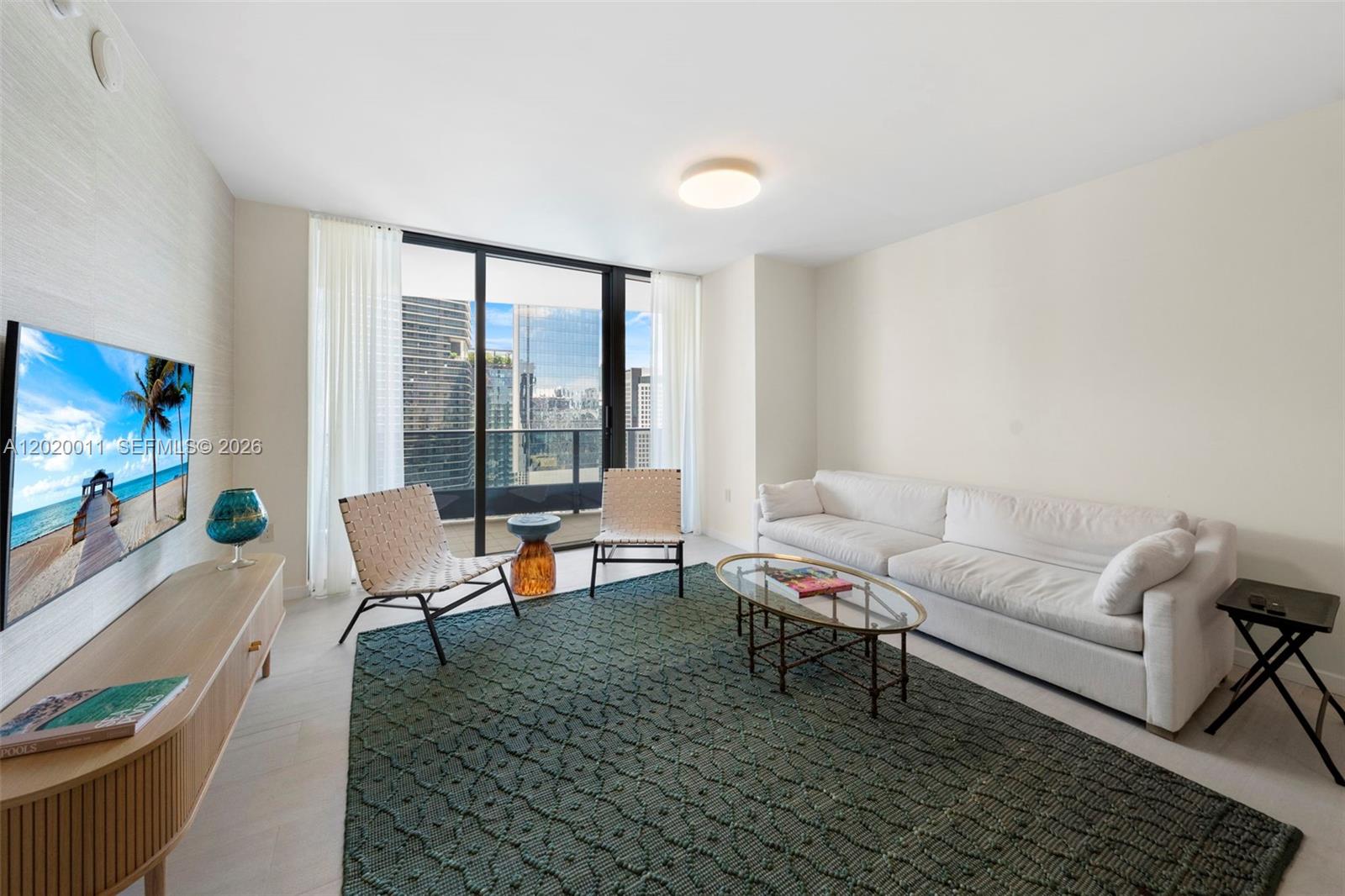 A living room features a white sofa, two woven chairs, a glass coffee table, and balcony — 1000 Brickell Plz # 4014, Miami FL 33131, MIAMI, FL