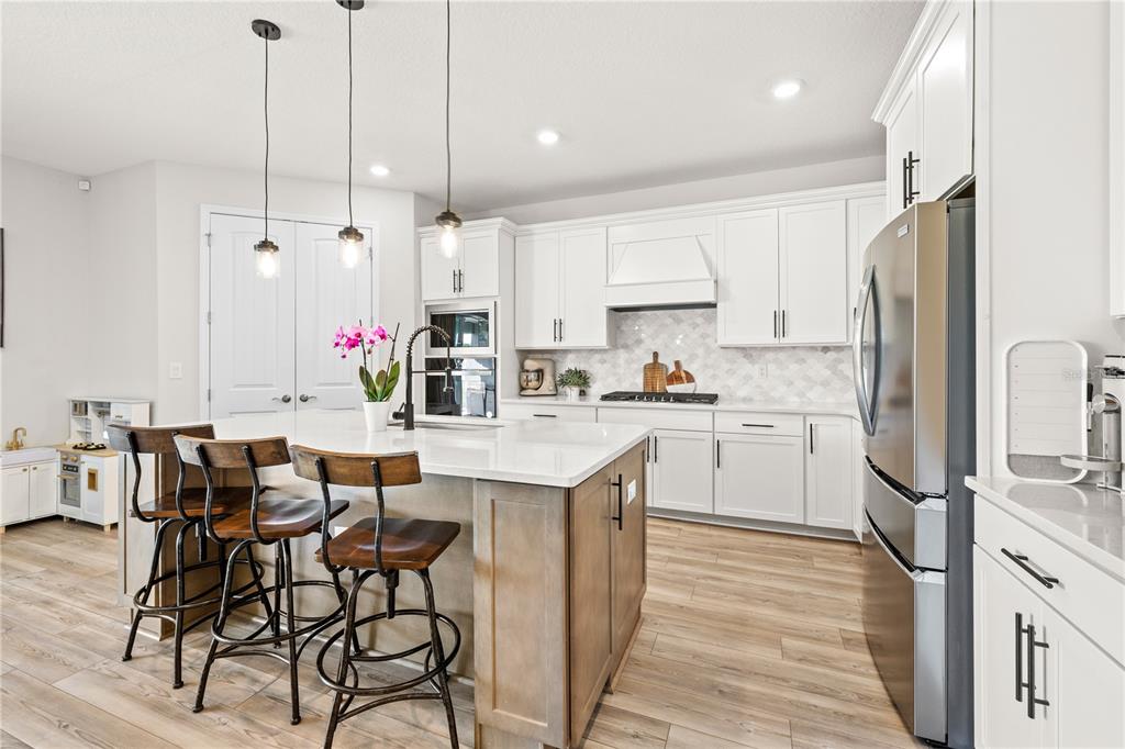 A modern kitchen features white cabinets, a wood-toned island with bar seating, and stainless appliances — 5269 FOOTHILLS PRESERVE LOOP, MOUNT DORA, FL