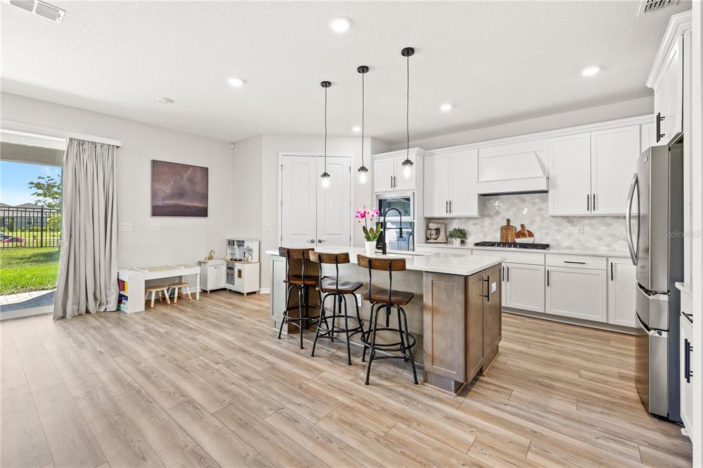 A kitchen features white cabinetry, a central island with bar stools, and light wood flooring — 5269 FOOTHILLS PRESERVE LOOP, MOUNT DORA, FL