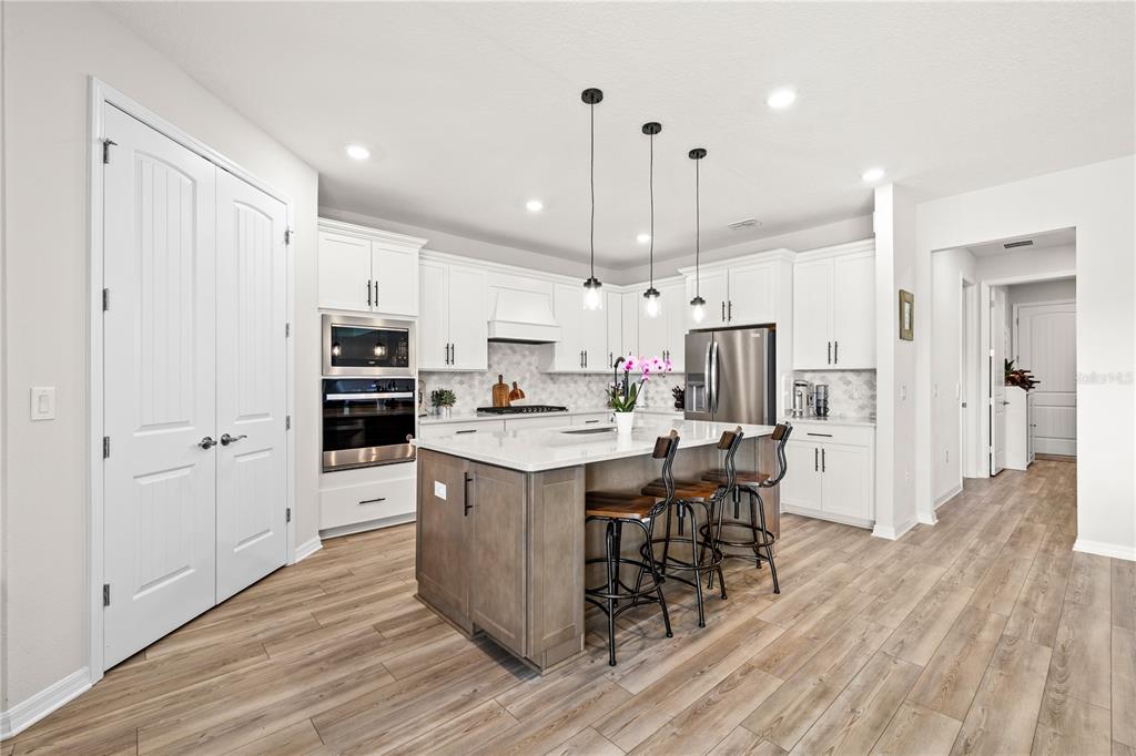 A modern kitchen features white cabinets, a gray island with bar seating, and wood flooring — 5269 FOOTHILLS PRESERVE LOOP, MOUNT DORA, FL