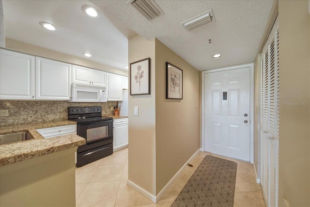 A kitchen with white cabinets and granite countertops sits beside an entryway with a door — 835 WEXFORD BOULEVARD UNIT 301, VENICE, FL