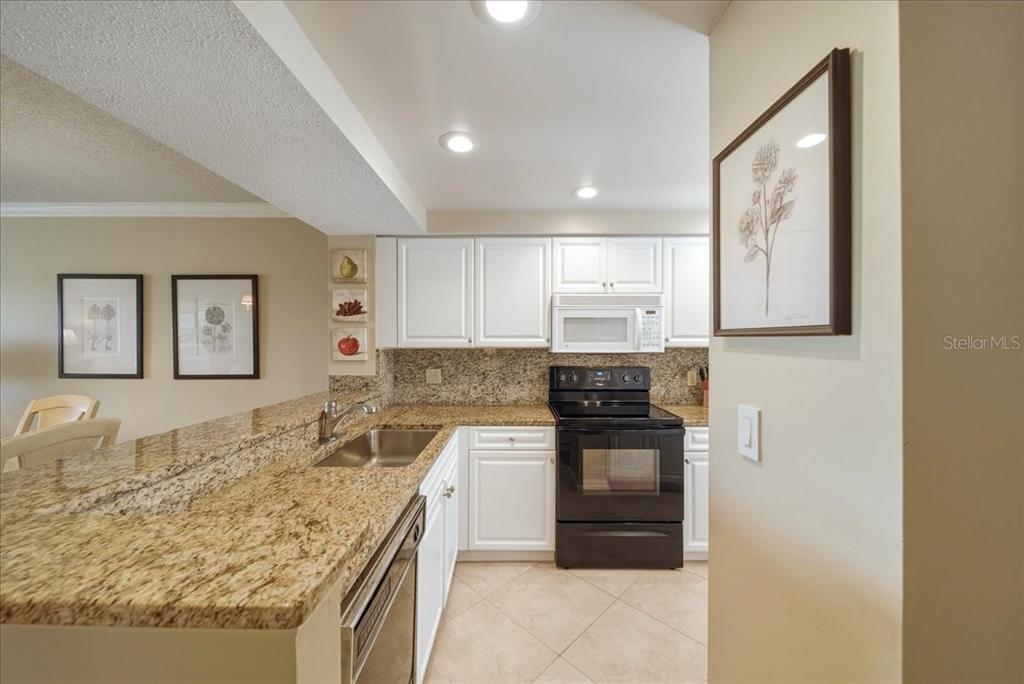 A kitchen features white cabinets, granite countertops, a black stove, and tile flooring — 835 WEXFORD BOULEVARD UNIT 301, VENICE, FL