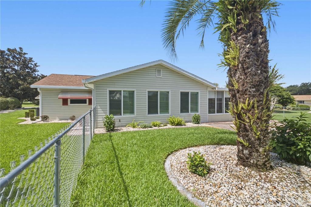 A light-colored, single-story house exterior features a chain-link fence, a palm tree, and landscaping — 17676 SE 102ND CIRCLE, SUMMERFIELD, FL