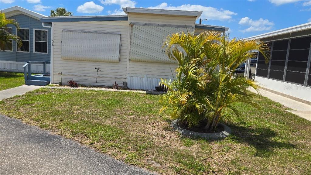 A light-colored mobile home features metal window awnings and a palm tree in the yard — 1475 FLAMINGO DRIVE UNIT 56, ENGLEWOOD, FL