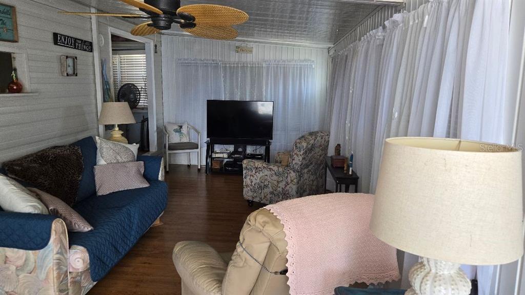 A living room features a blue sofa, floral armchair, television, and white curtains — 1475 FLAMINGO DRIVE UNIT 56, ENGLEWOOD, FL