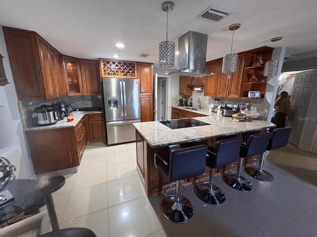 A kitchen features wood cabinets, granite countertops, a center island with seating, and stainless appliances — 6005 W CLIFTON STREET, TAMPA, FL