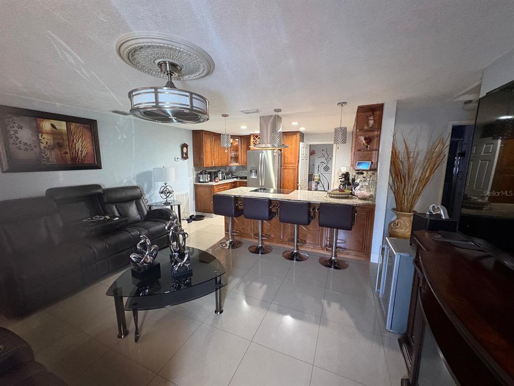 An open-concept living room features a black leather sofa, a kitchen island, and tile flooring — 6005 W CLIFTON STREET, TAMPA, FL