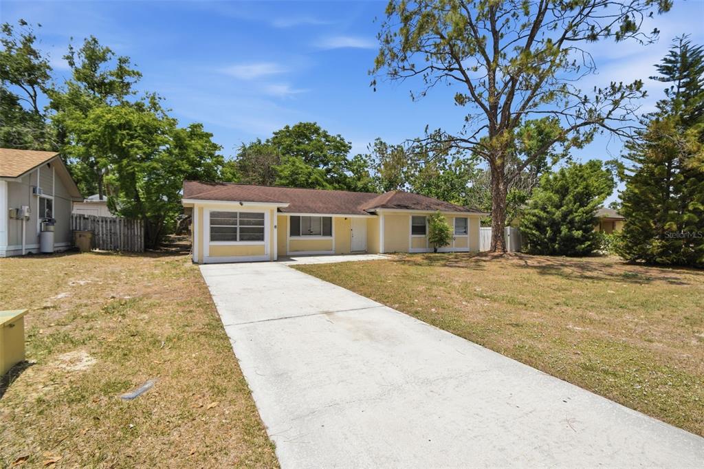 A single-story yellow house with a concrete driveway and a large tree in the yard — 8412 RENALD BOULEVARD, TAMPA, FL