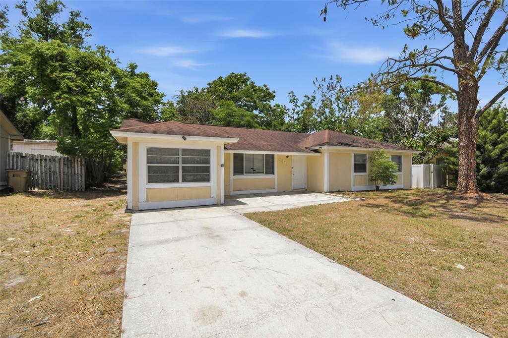 A single-story yellow house with a concrete driveway and a brown shingled roof — 8412 RENALD BOULEVARD, TAMPA, FL