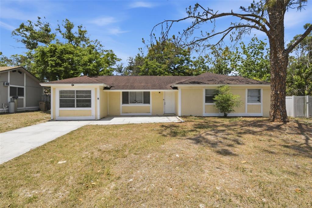 A single-story yellow house with a brown roof and a concrete driveway — 8412 RENALD BOULEVARD, TAMPA, FL