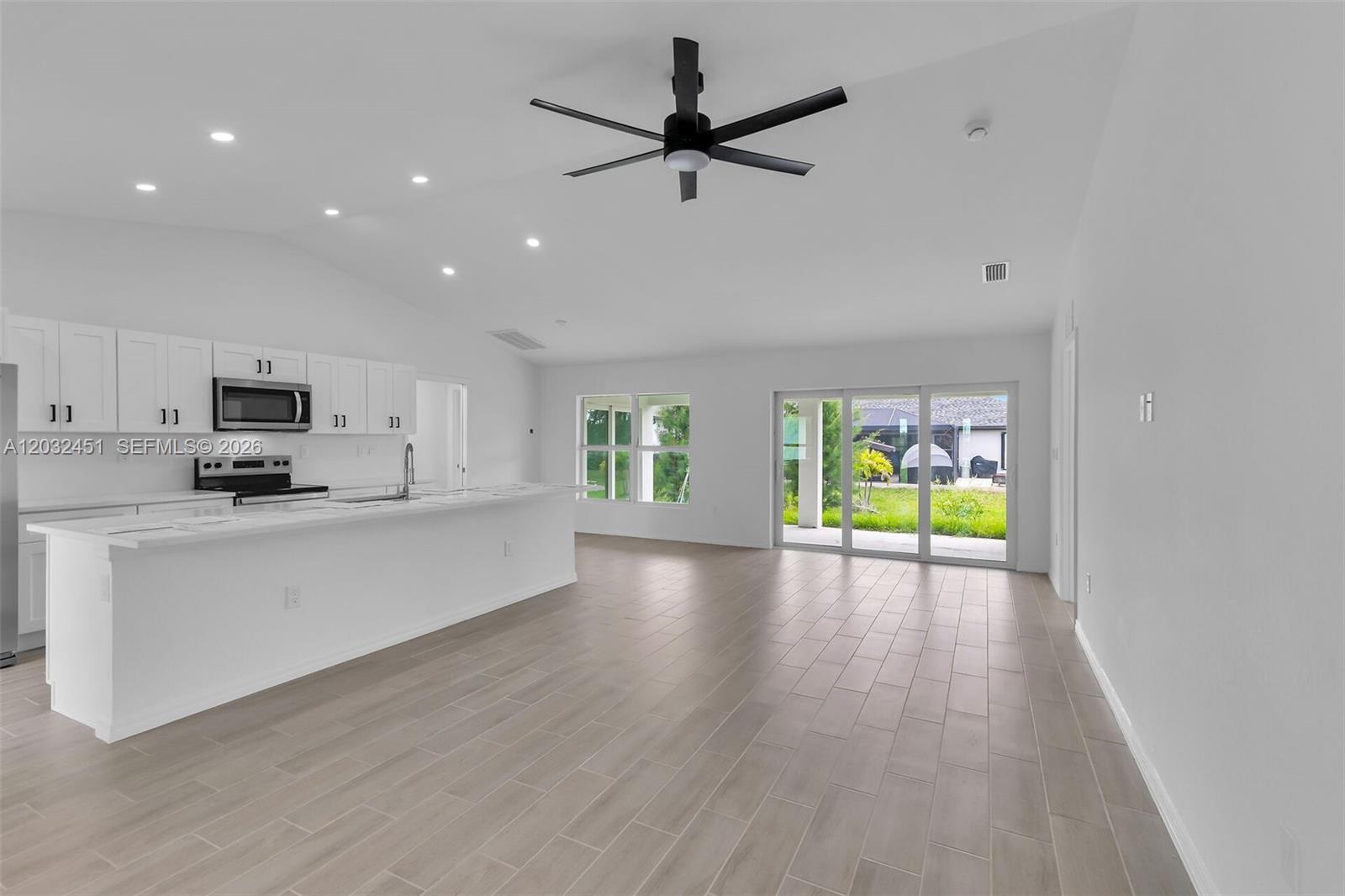 A modern kitchen with white cabinets and an island opens into a spacious living area — 2221 NW 43rd, Cape Coral FL 33993, CAPE CORAL, FL