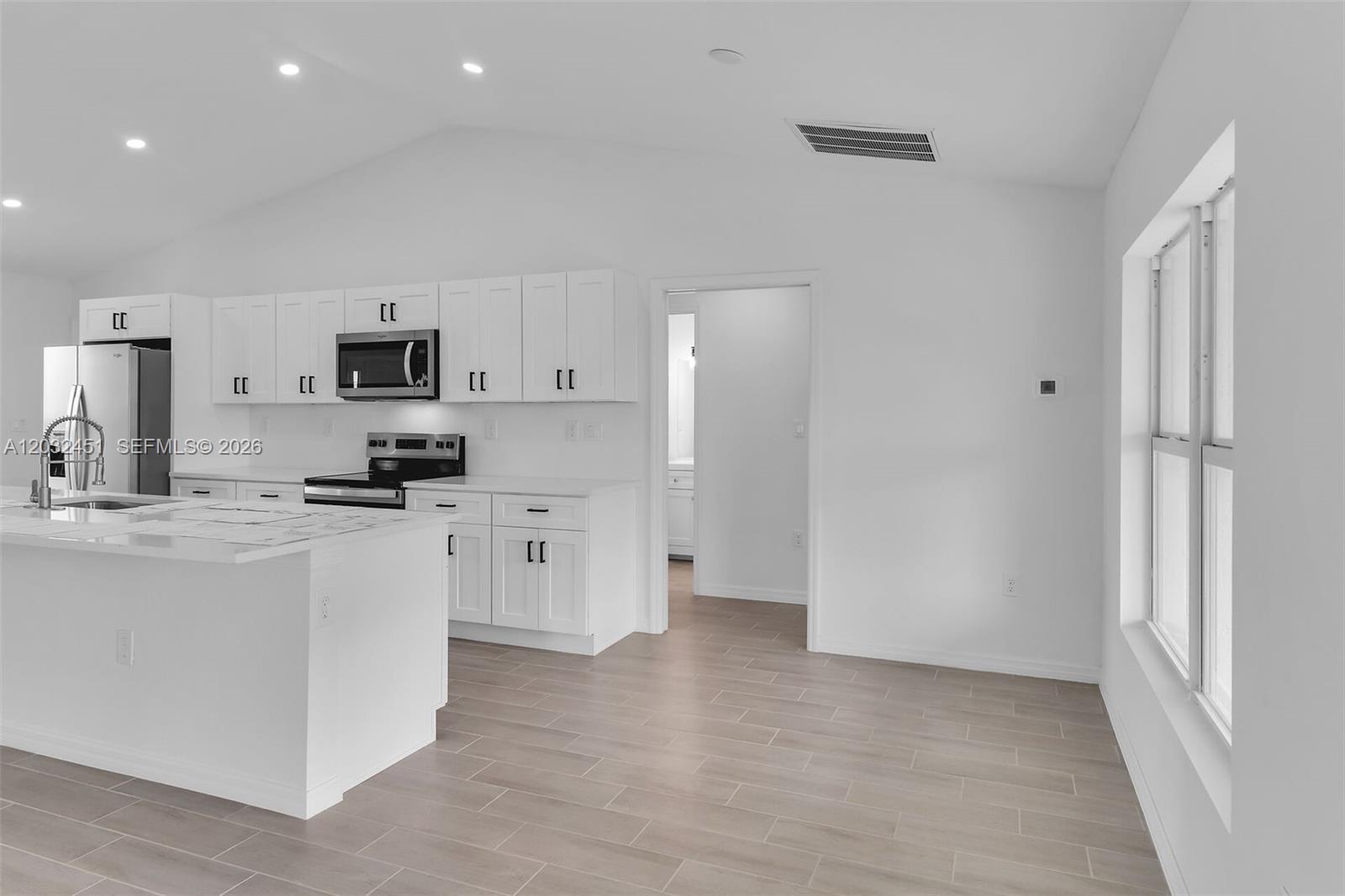 A modern kitchen features white cabinetry, stainless steel appliances, and a large central island — 2221 NW 43rd, Cape Coral FL 33993, CAPE CORAL, FL