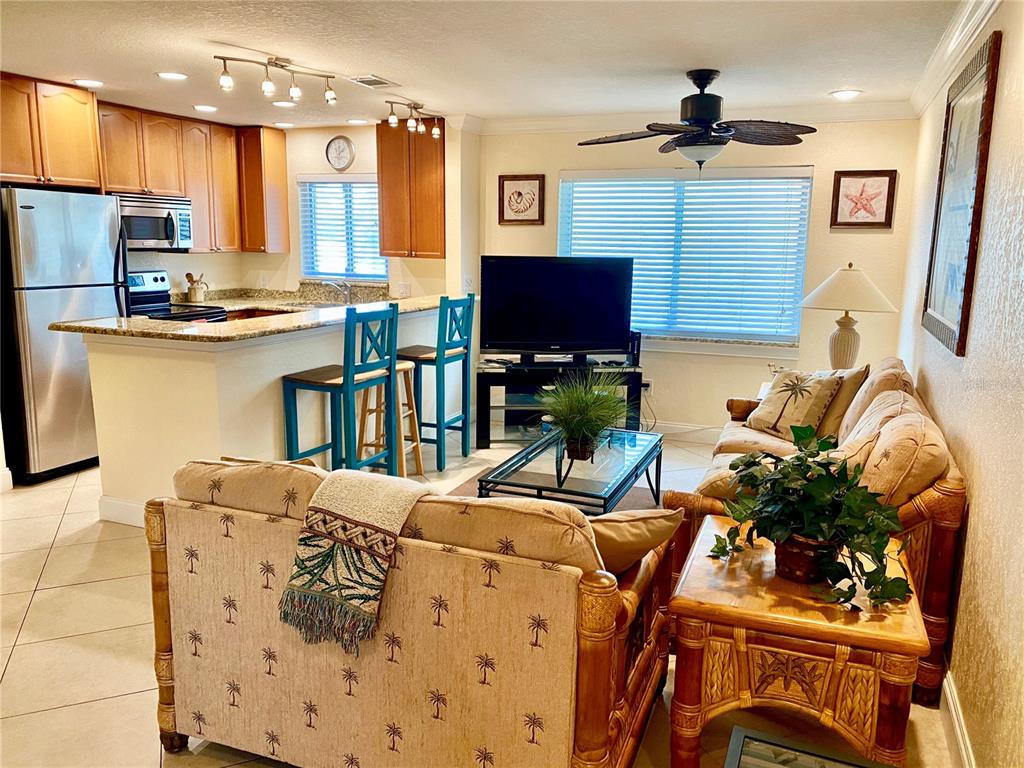 An open-concept living room and kitchen featuring rattan furniture, a breakfast bar, and tile floors — 9060 BLIND PASS ROAD UNIT 25, ST PETE BEACH, FL