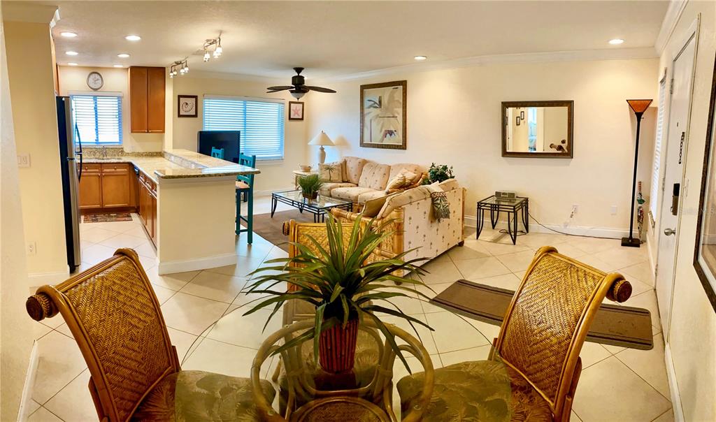 An open-concept living and dining area features tile floors, wicker furniture, and a kitchen island — 9060 BLIND PASS ROAD UNIT 25, ST PETE BEACH, FL