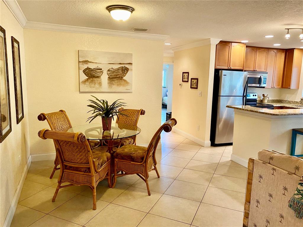 A dining area with a glass table and wicker chairs sits adjacent to a kitchen — 9060 BLIND PASS ROAD UNIT 25, ST PETE BEACH, FL