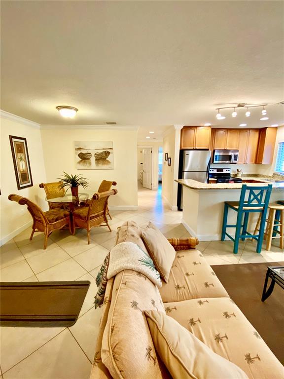 This open-concept living area features a dining set, a sofa, and a kitchen with bar seating — 9060 BLIND PASS ROAD UNIT 25, ST PETE BEACH, FL