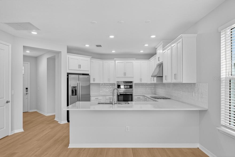 A kitchen features white cabinets, stainless steel appliances, and light wood-look flooring — 6932 PRAIRIE OAK WAY, NOKOMIS, FL