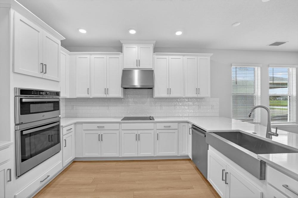 A modern kitchen features white cabinets, stainless steel appliances, a farmhouse sink, and light flooring — 6932 PRAIRIE OAK WAY, NOKOMIS, FL