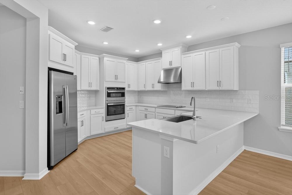 A modern kitchen features white cabinets, stainless steel appliances, and a quartz-topped island — 6932 PRAIRIE OAK WAY, NOKOMIS, FL
