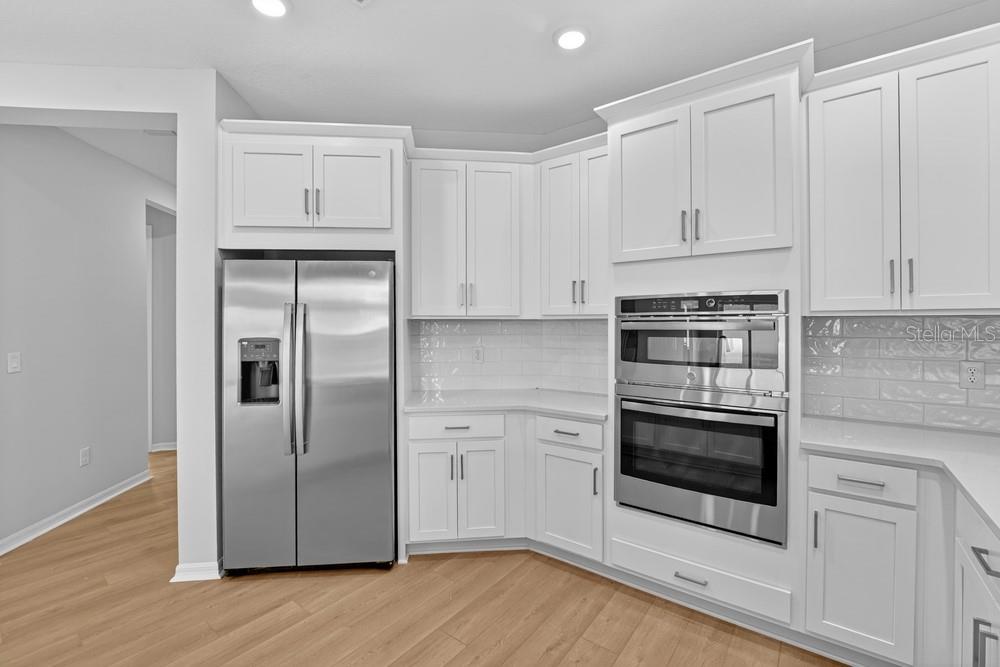 A modern kitchen features white cabinets, quartz countertops, a farmhouse sink, and stainless steel appliances — 6932 PRAIRIE OAK WAY, NOKOMIS, FL