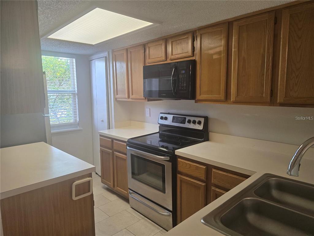 A kitchen features wood cabinets, white countertops, stainless steel appliances, and a window — 8713 LIBERTY PLACE, TAMPA, FL