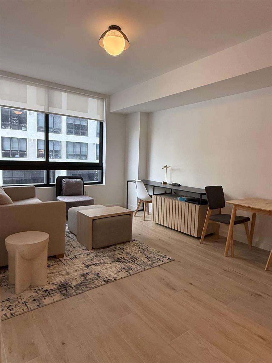 A modern living room features light wood flooring, a neutral sofa, and a long desk — 225 N Miami Avenue # 910, Miami FL 33128, MIAMI, FL