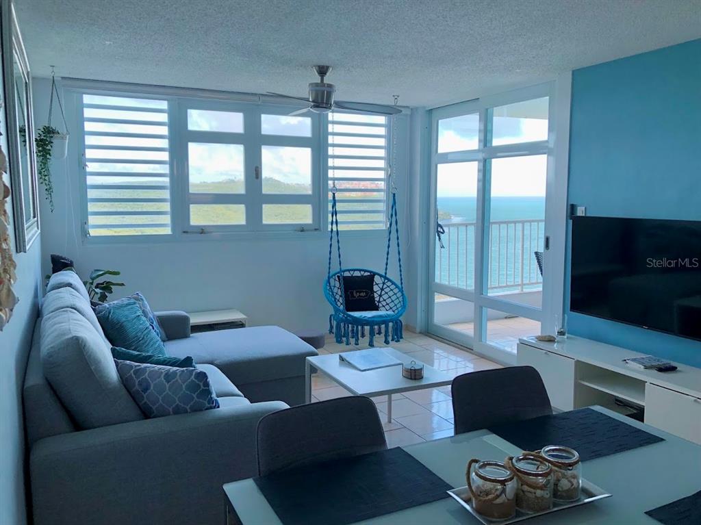 A living room with a blue accent wall, sectional sofa, hanging chair, and ocean view — 200 MARINA VIEW DOS MARINAS II CONDOMINIUM UNIT 2103, FAJARDO, PR