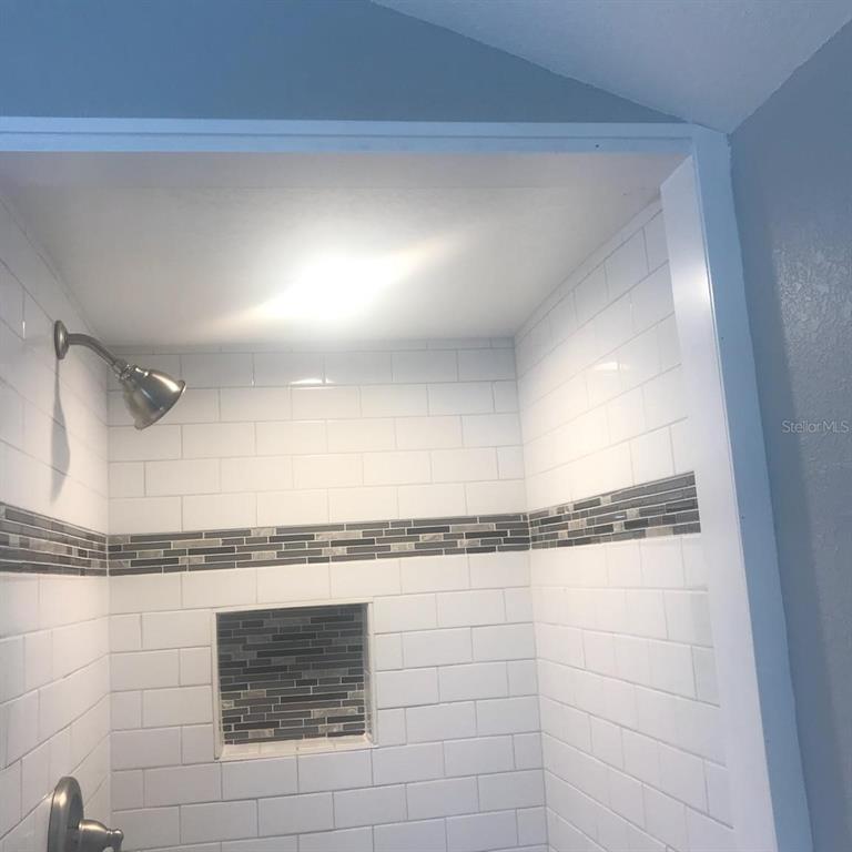 A shower stall features white subway tiles, a gray mosaic accent strip, and a recessed niche — 1000 10TH AVENUE NW UNIT 3, LARGO, FL