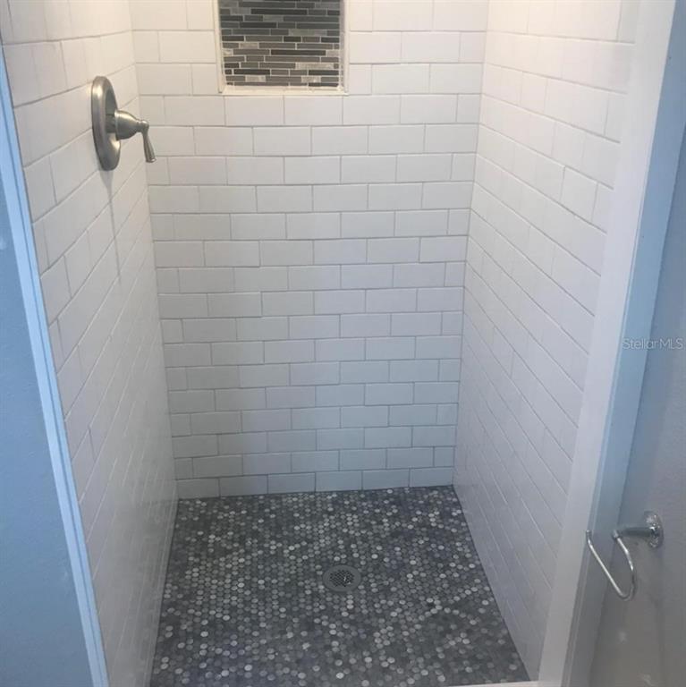A walk-in shower features white subway tile walls, a gray pebble floor, and a niche — 1000 10TH AVENUE NW UNIT 3, LARGO, FL