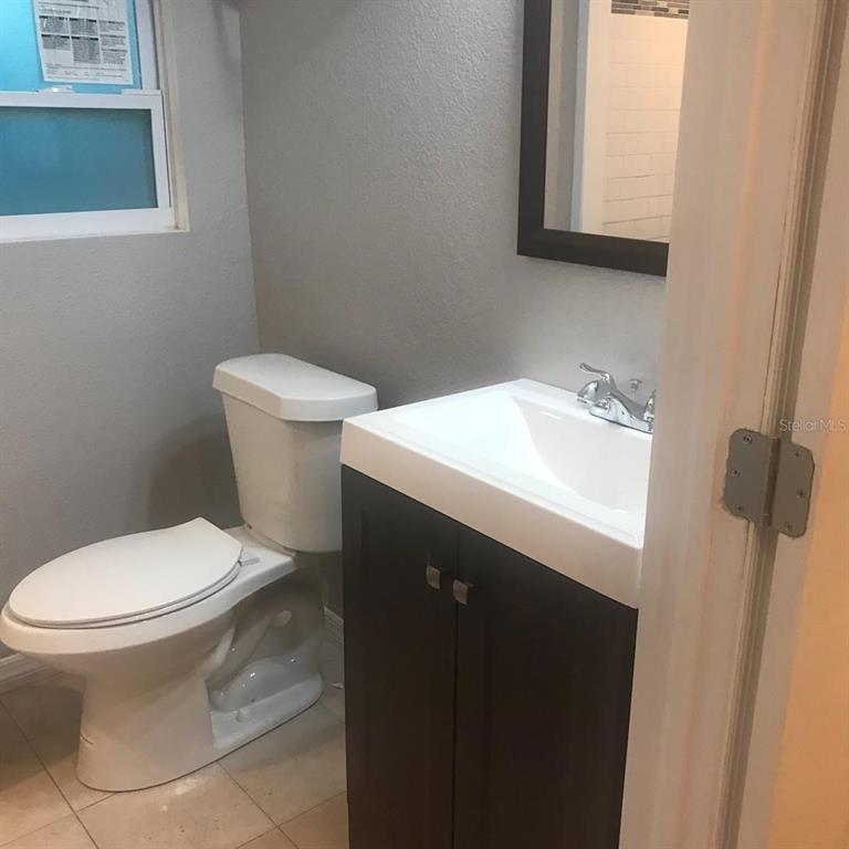 A small bathroom features a white toilet, a dark wood vanity, and a wall mirror — 1000 10TH AVENUE NW UNIT 3, LARGO, FL